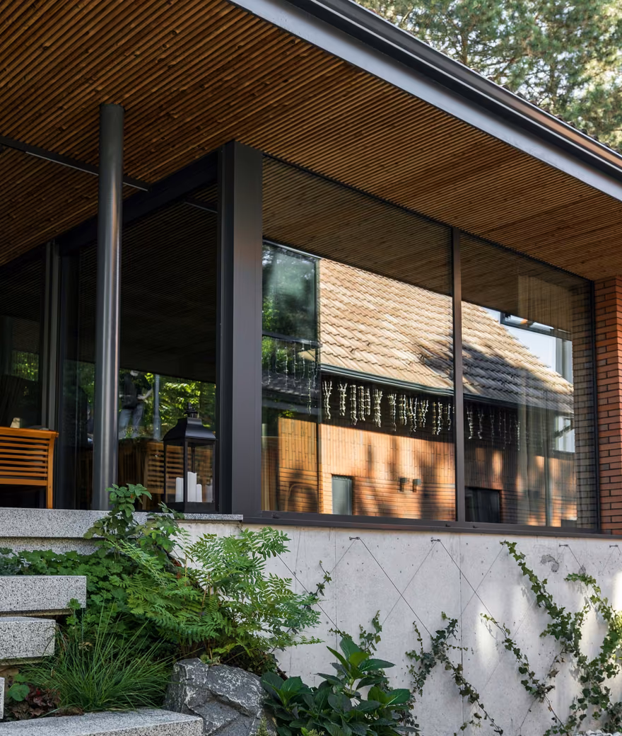 Contemporary brick house with a timber-covered terrace and panoramic glazing overlooking the garden.