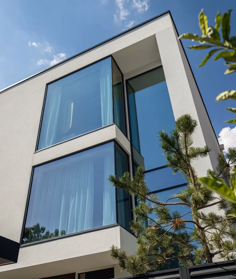 Front facade of a contemporary house with panoramic glazing, white architectural volumes and dark window frames.