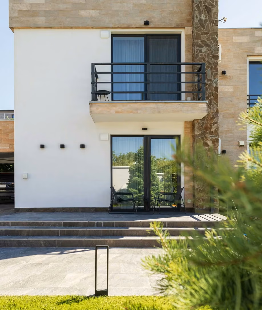 Contemporary house with a light-coloured façade, stone cladding and panoramic windows with dark frames.