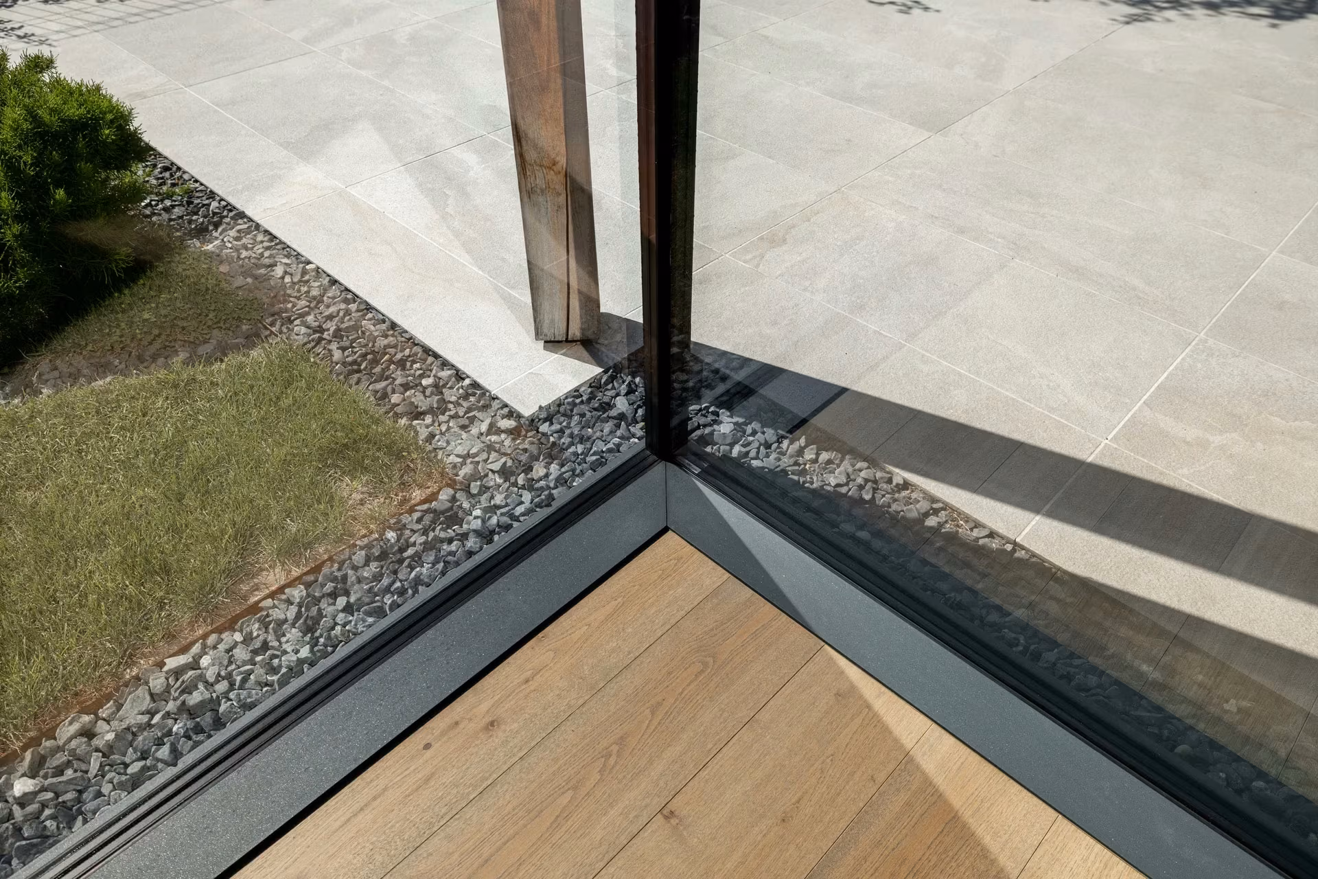 Floor-level panoramic glass corner between the wooden floor and outdoor terrace.