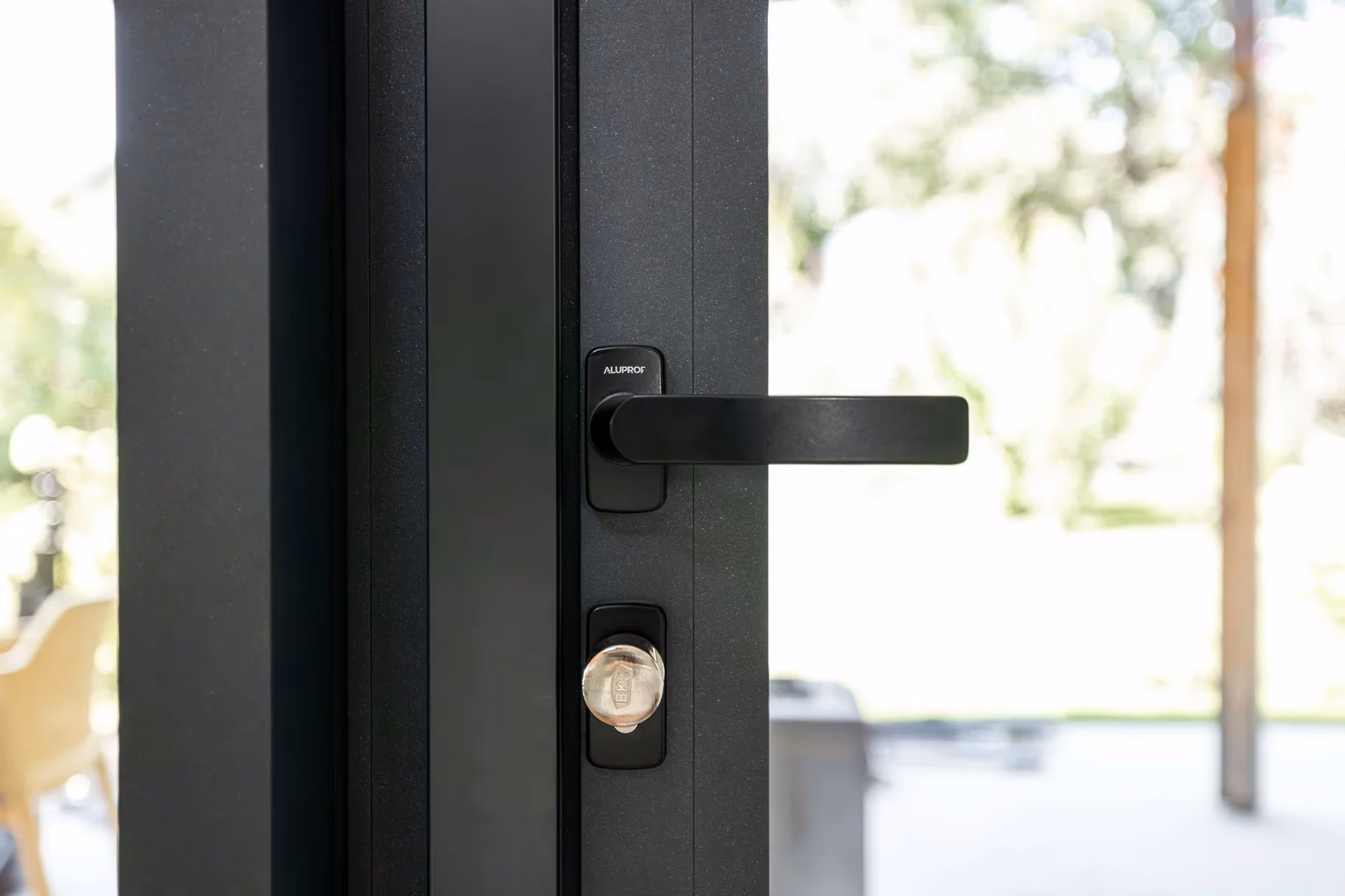 Close-up of a black door handle and key cylinder on an aluminium frame.
