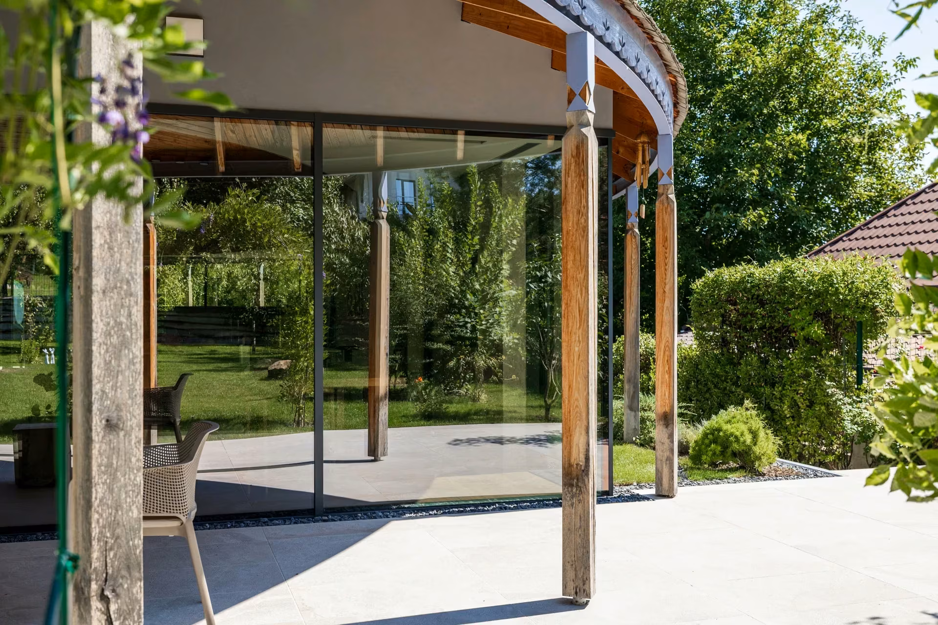 Curved section of the glazed facade with timber columns and surrounding greenery.