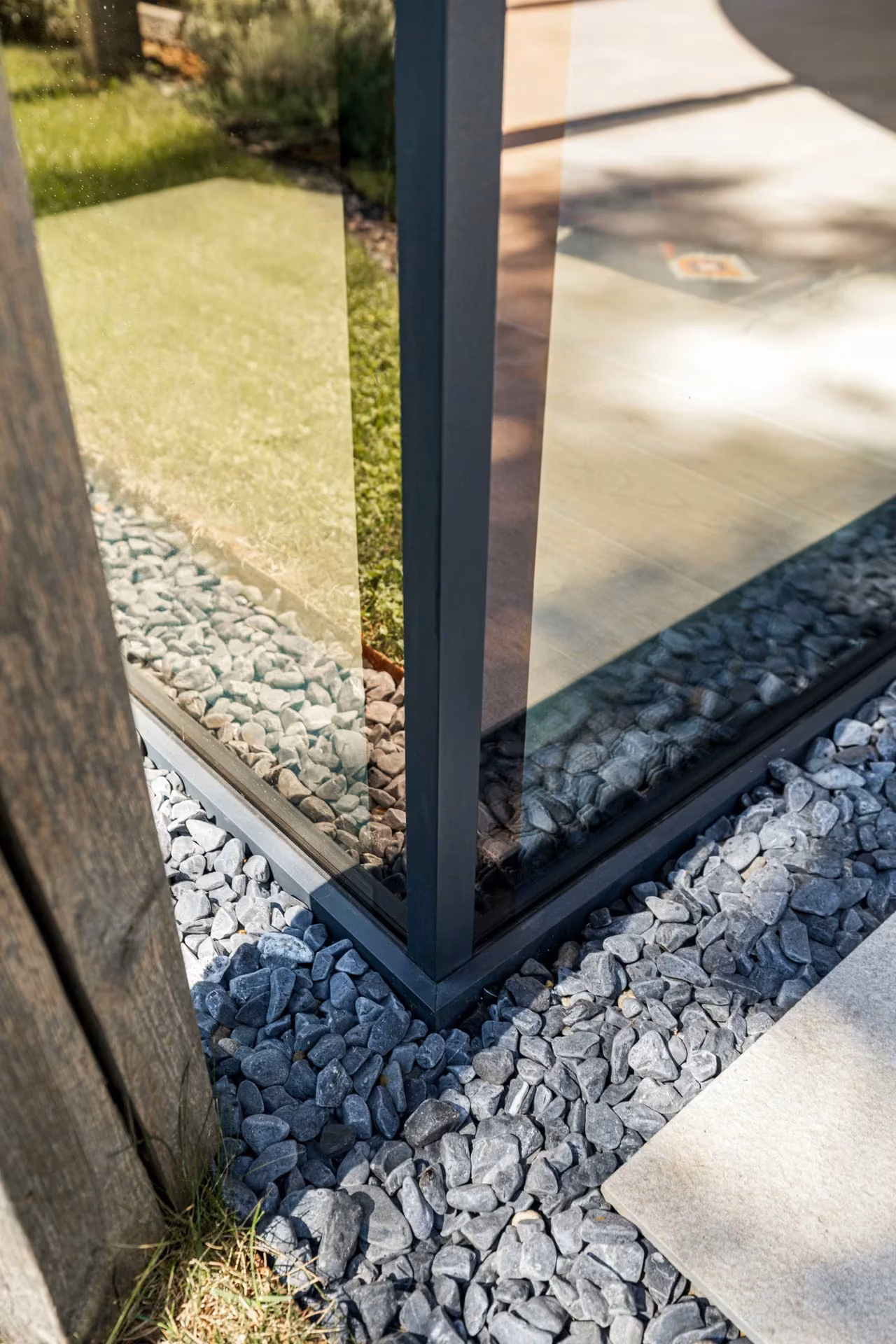 Exterior glass façade corner with an aluminium frame and gravel at its base.