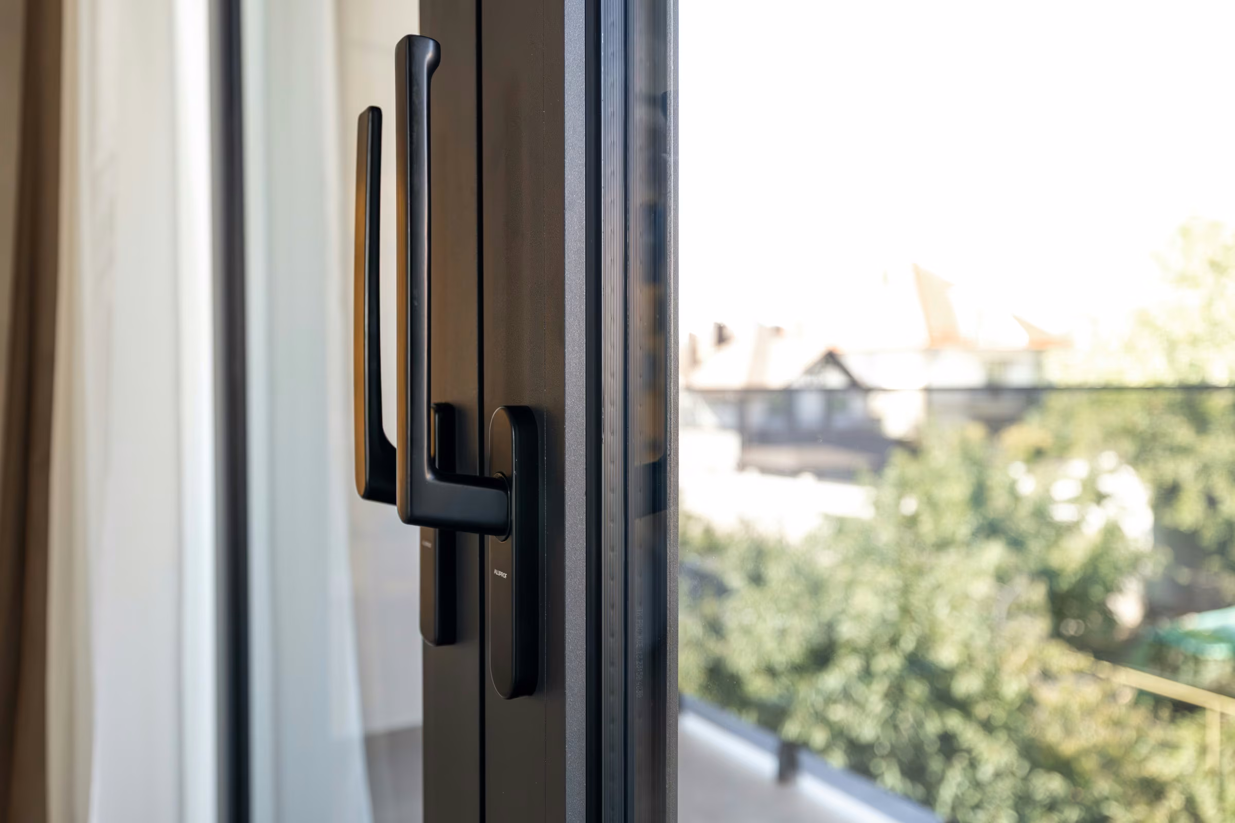Close-up of a black handle on a glazed door with greenery in the background.