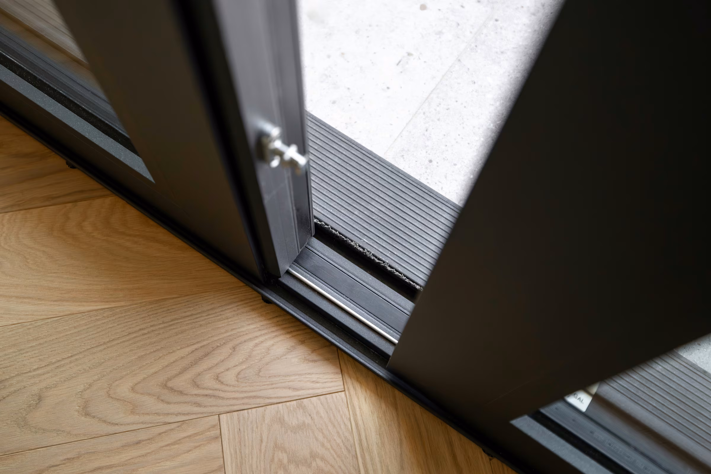 Detail of a glazed door threshold between timber flooring and the outdoor terrace.