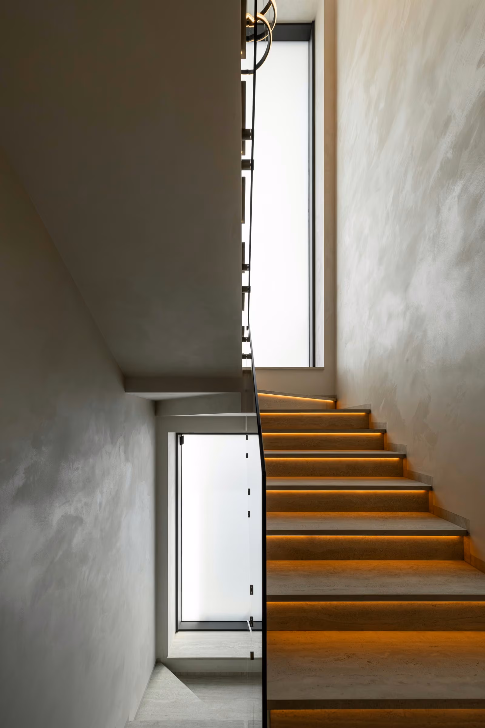 Interior timber staircase with illuminated steps and tall vertical windows.