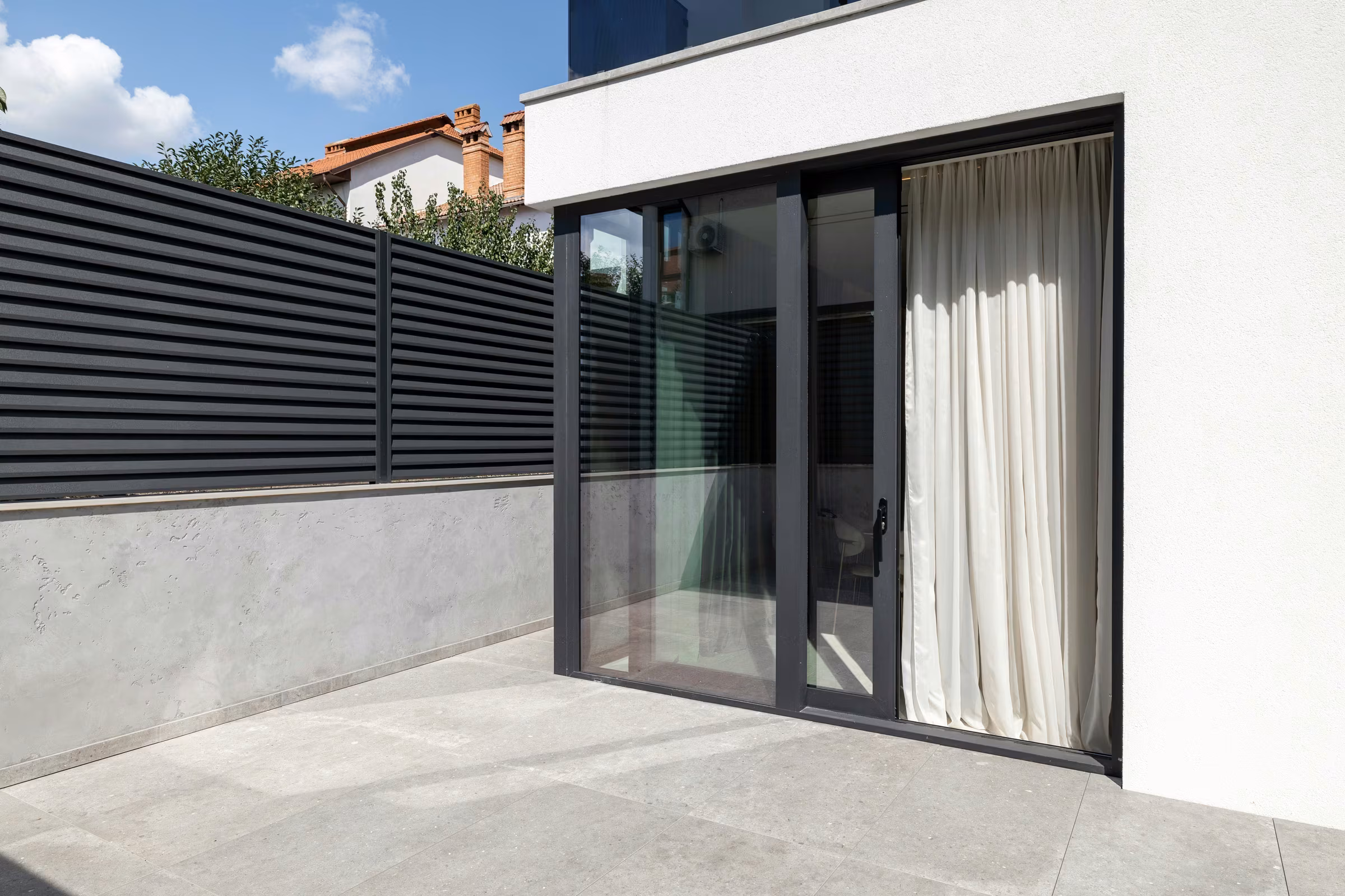 Outdoor terrace with a glazed sliding system and dark frames.