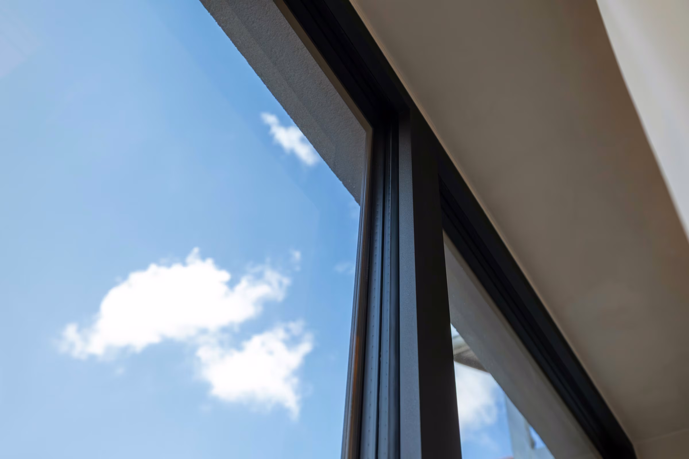 Detail of the upper corner of panoramic glazing reflecting the sky.