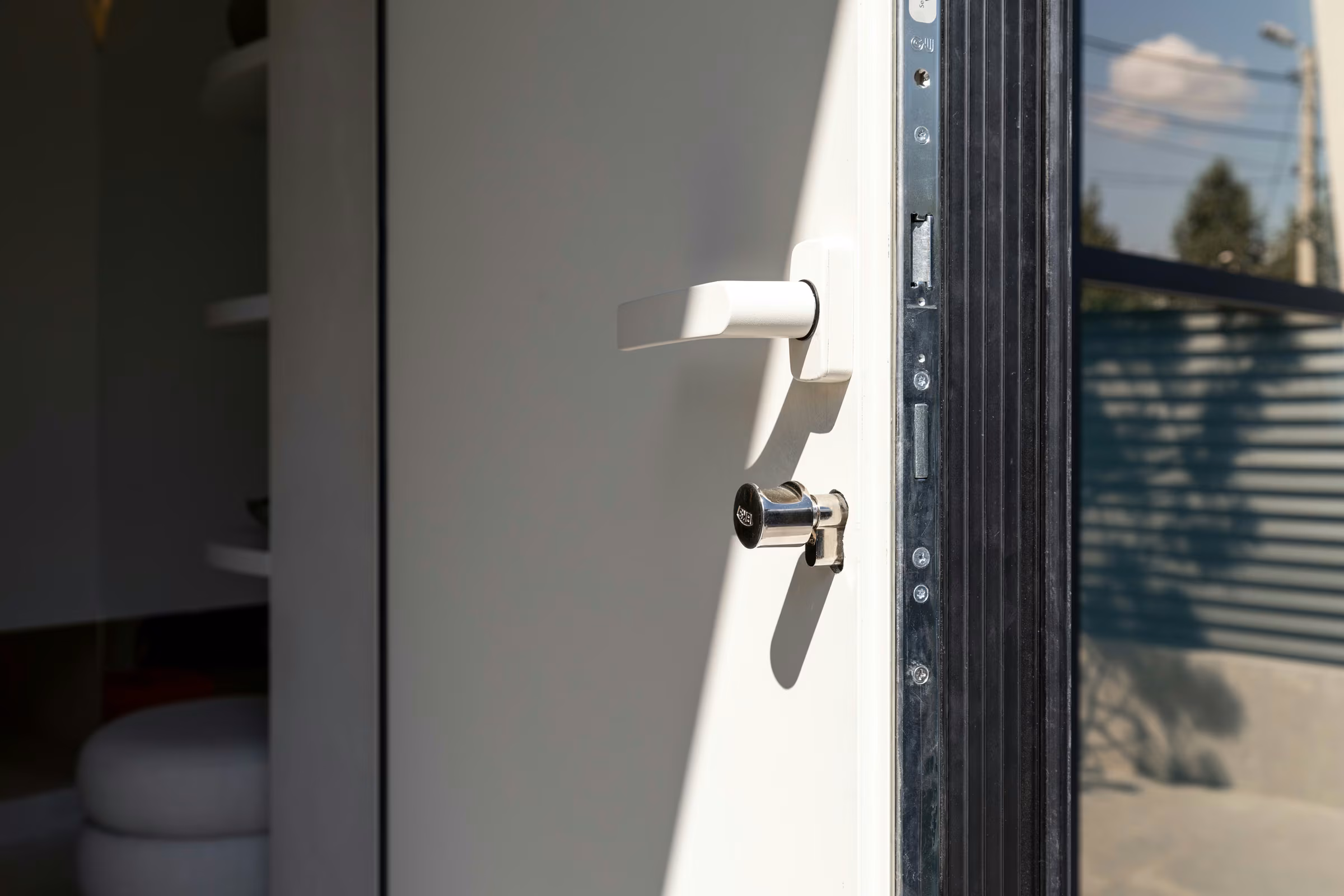 White door handle and lock cylinder on an open door leaf with a dark frame.