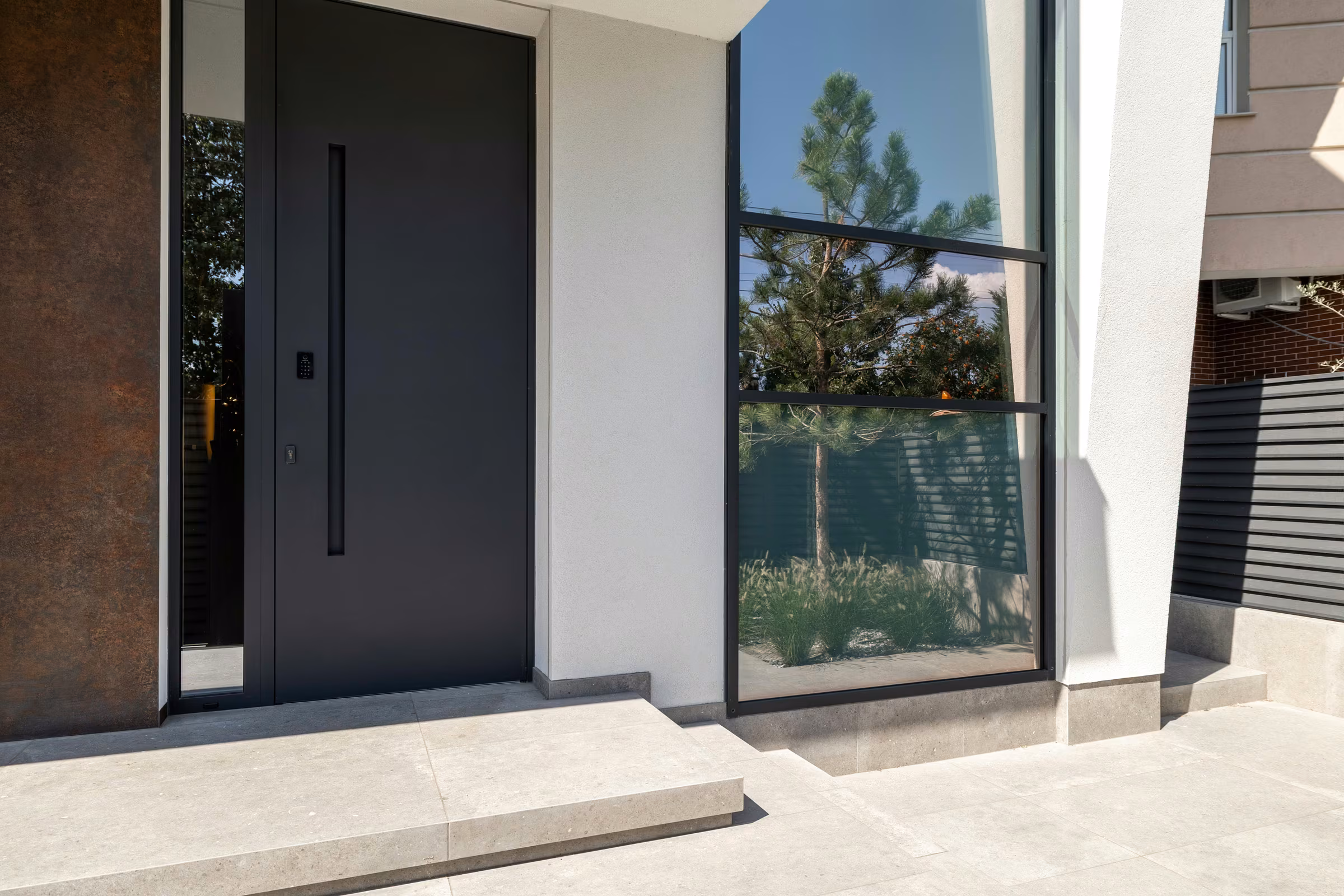 Dark entrance door beside a tall glazed panel and a textured façade.