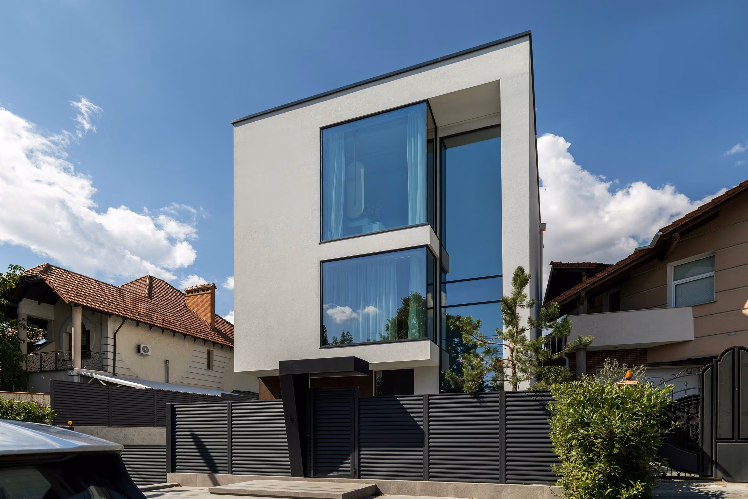 Contemporary house with a white façade, panoramic windows and a dark metal fence.