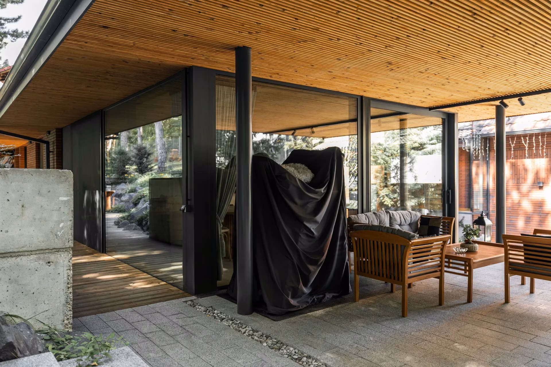 Covered terrace with a timber ceiling, outdoor seating and a glazed facade with dark frames.