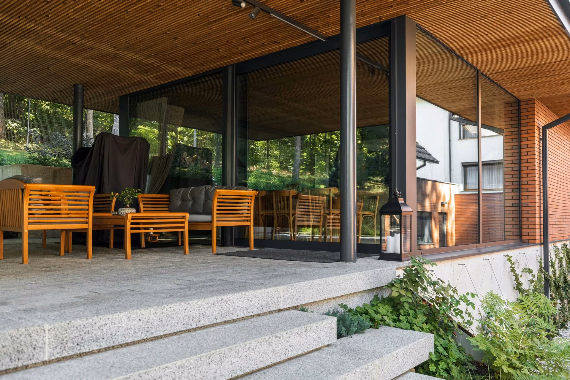 Terrace with timber chairs, stone steps and glazed surfaces on a brick façade.