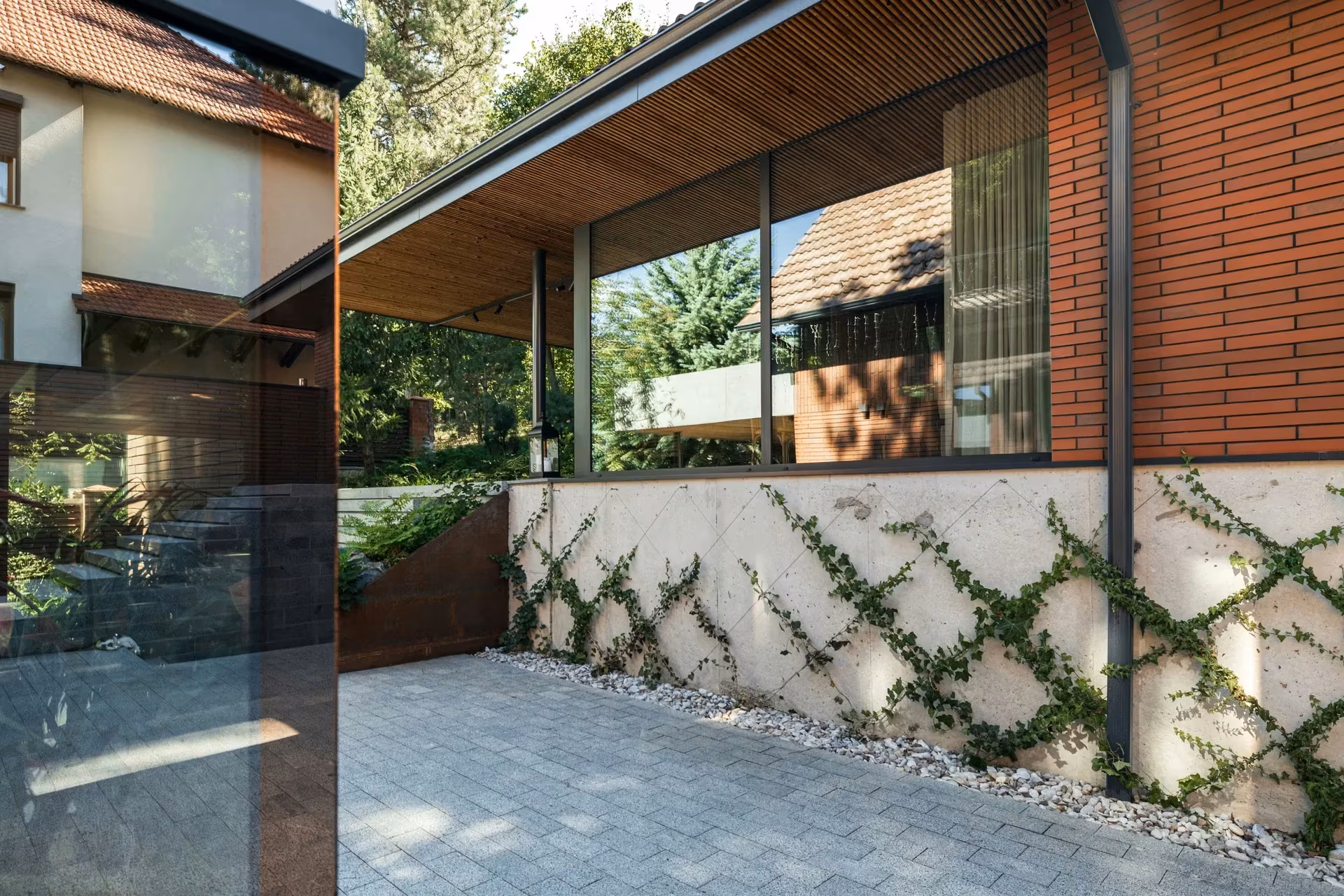 Paved walkway between brick façades and glass surfaces reflecting the garden.