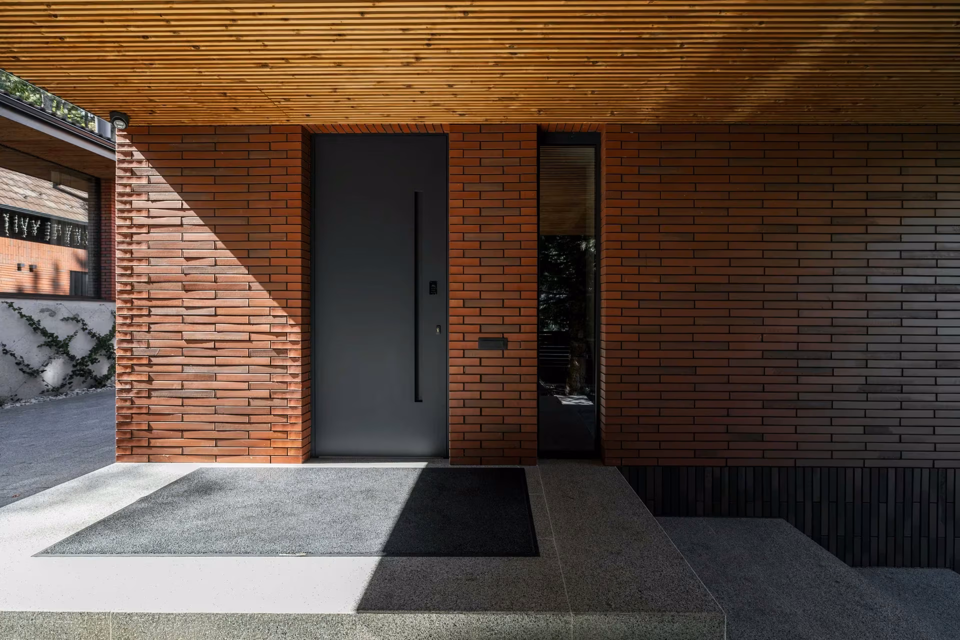 Dark entrance door integrated into a brick façade, with narrow side glazing.