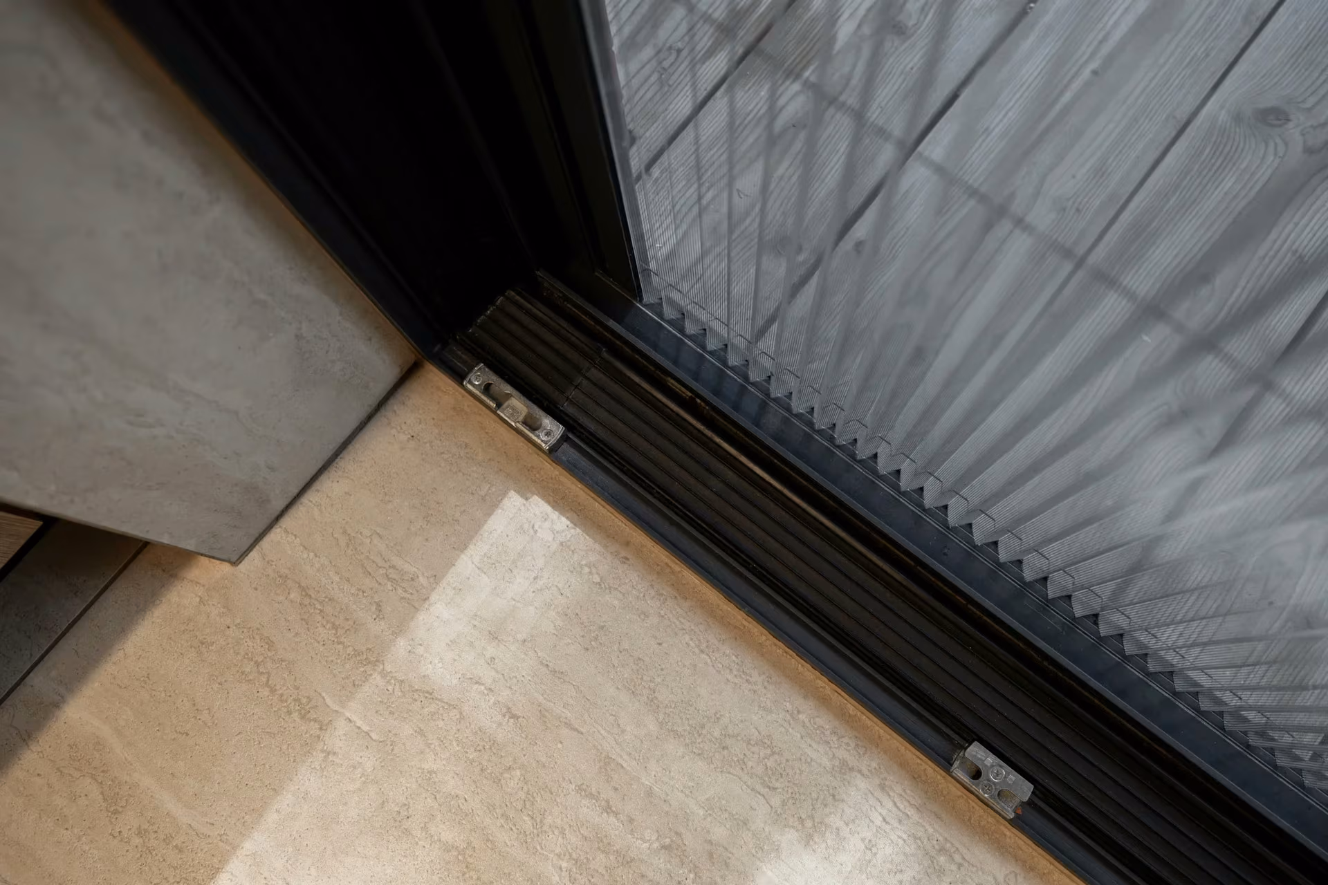 Detail of a glazed door threshold and lower frame beside timber flooring.