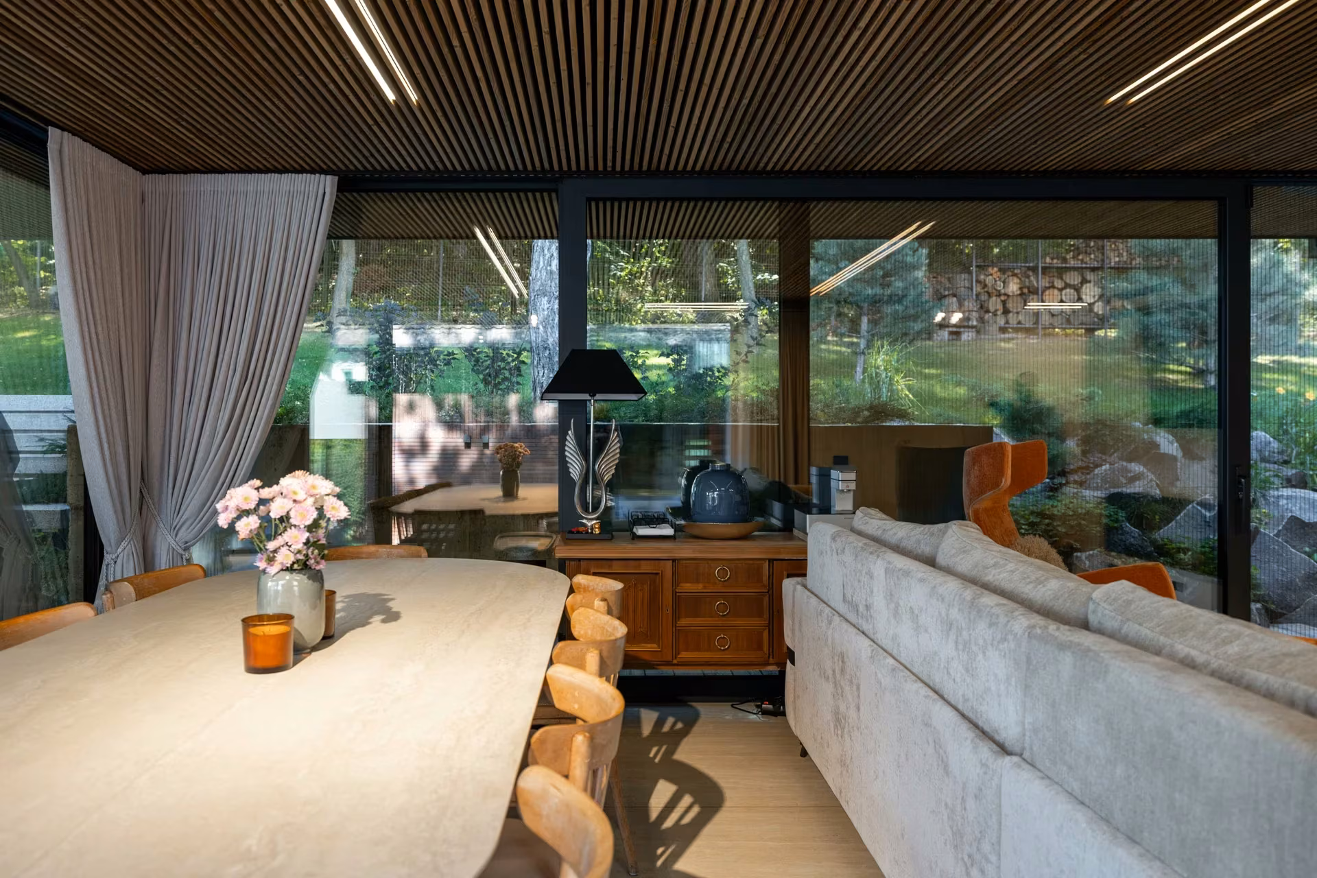 Dining area with an oval table, sofa and panoramic glazed doors facing the garden.
