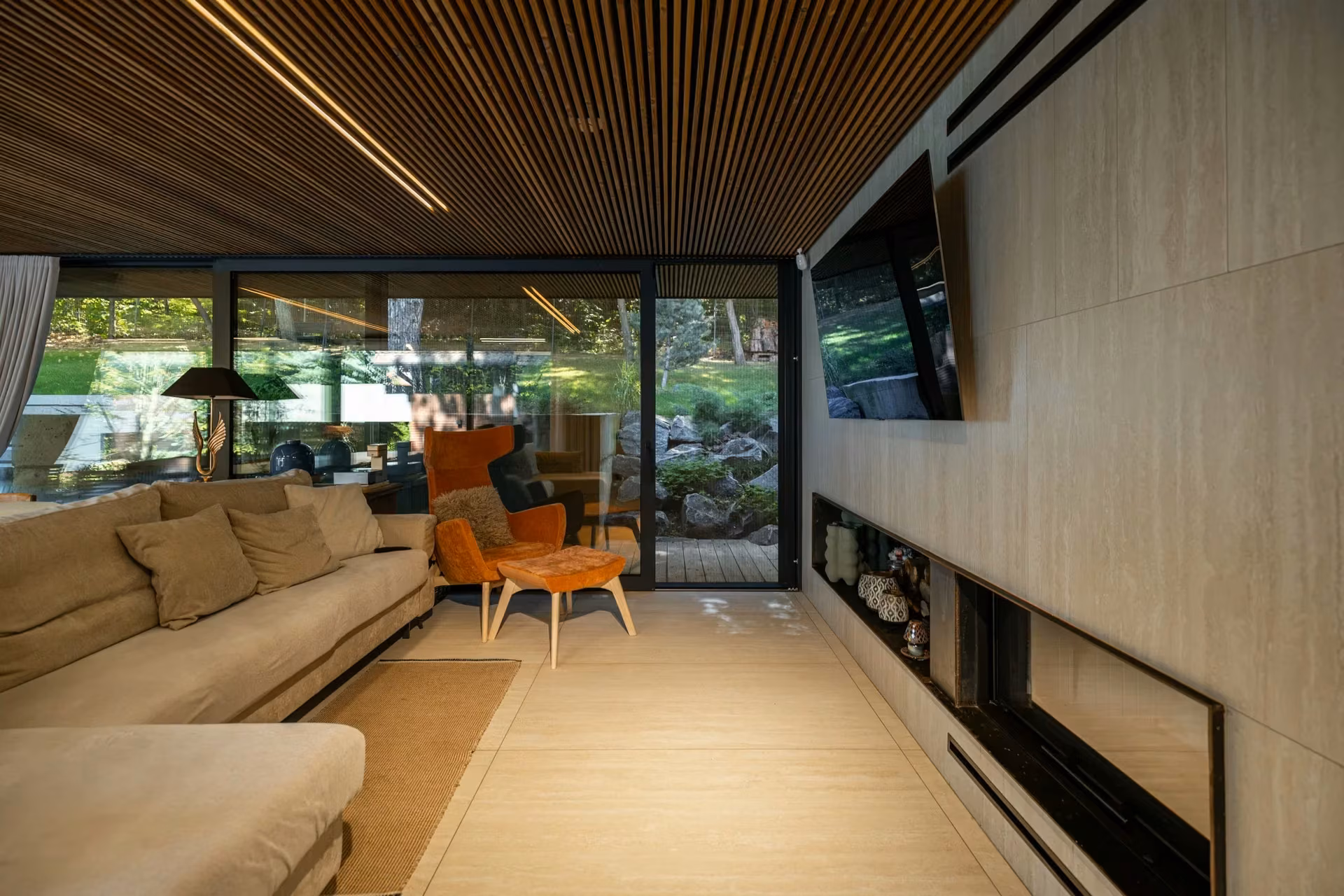 Long living room with a sofa, fireplace and glazed wall facing the outdoor terrace.