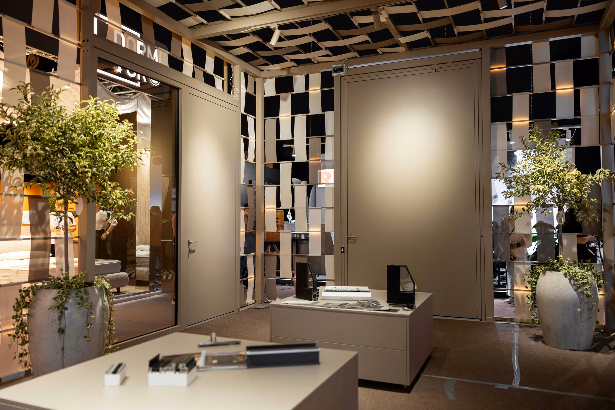 Interior of the Plastregal stand with a large neutral-toned door, display furniture and decorative plants.