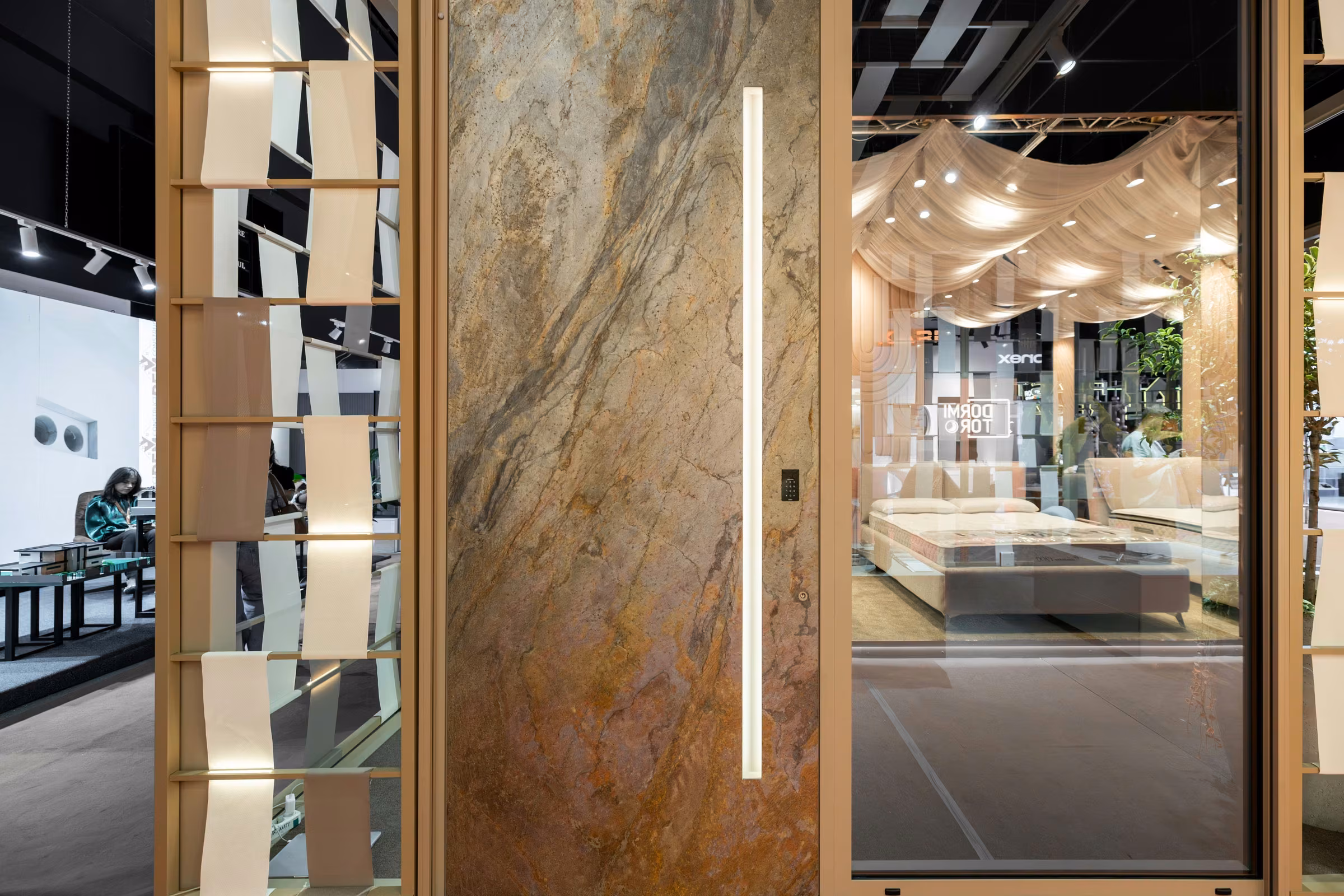 Tall door with a stone-look panel and elongated vertical handle, integrated into the exhibition frontage.