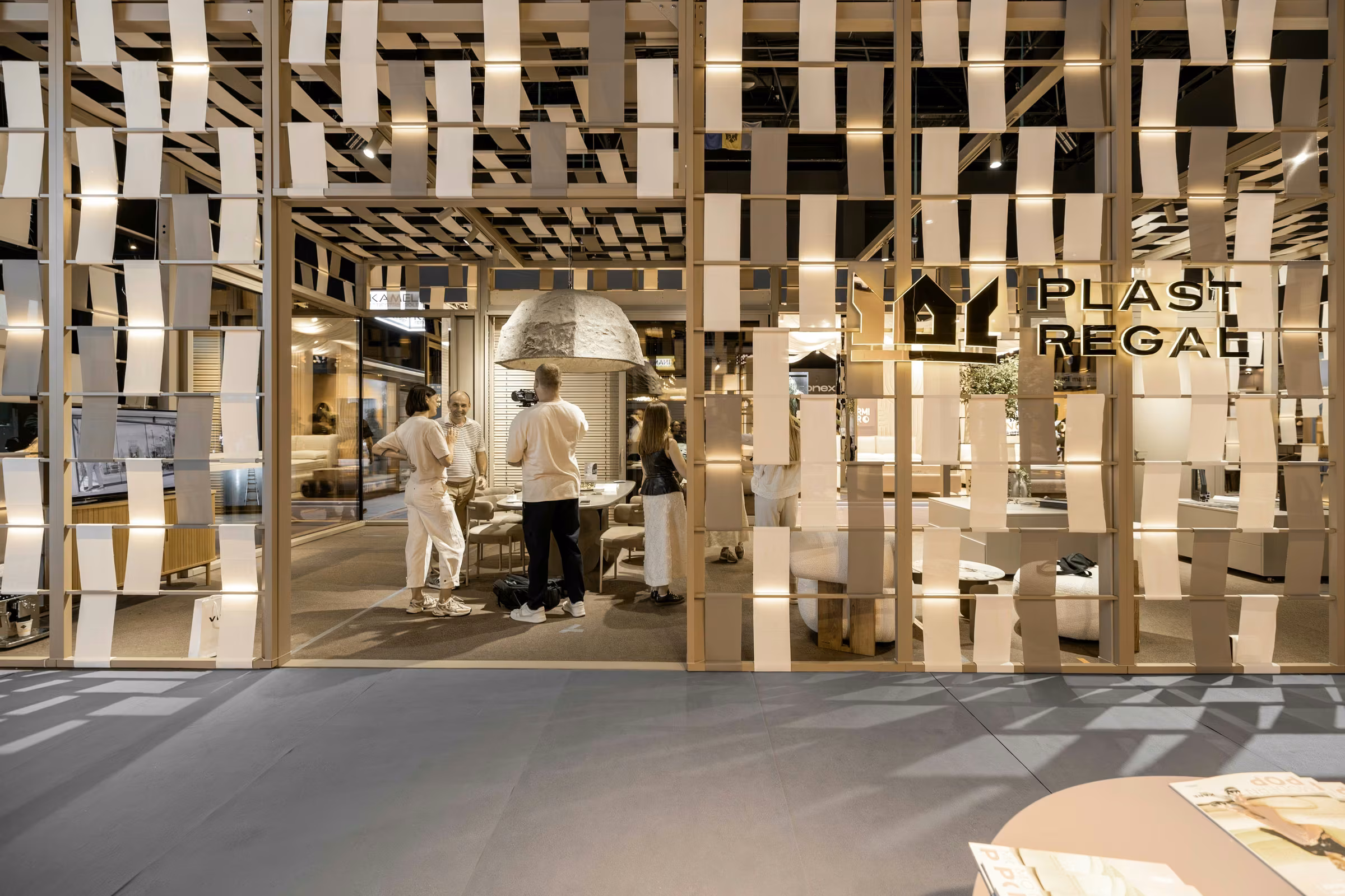 Main frontage of the Plastregal stand with a geometric timber structure and the brand logo visible inside.