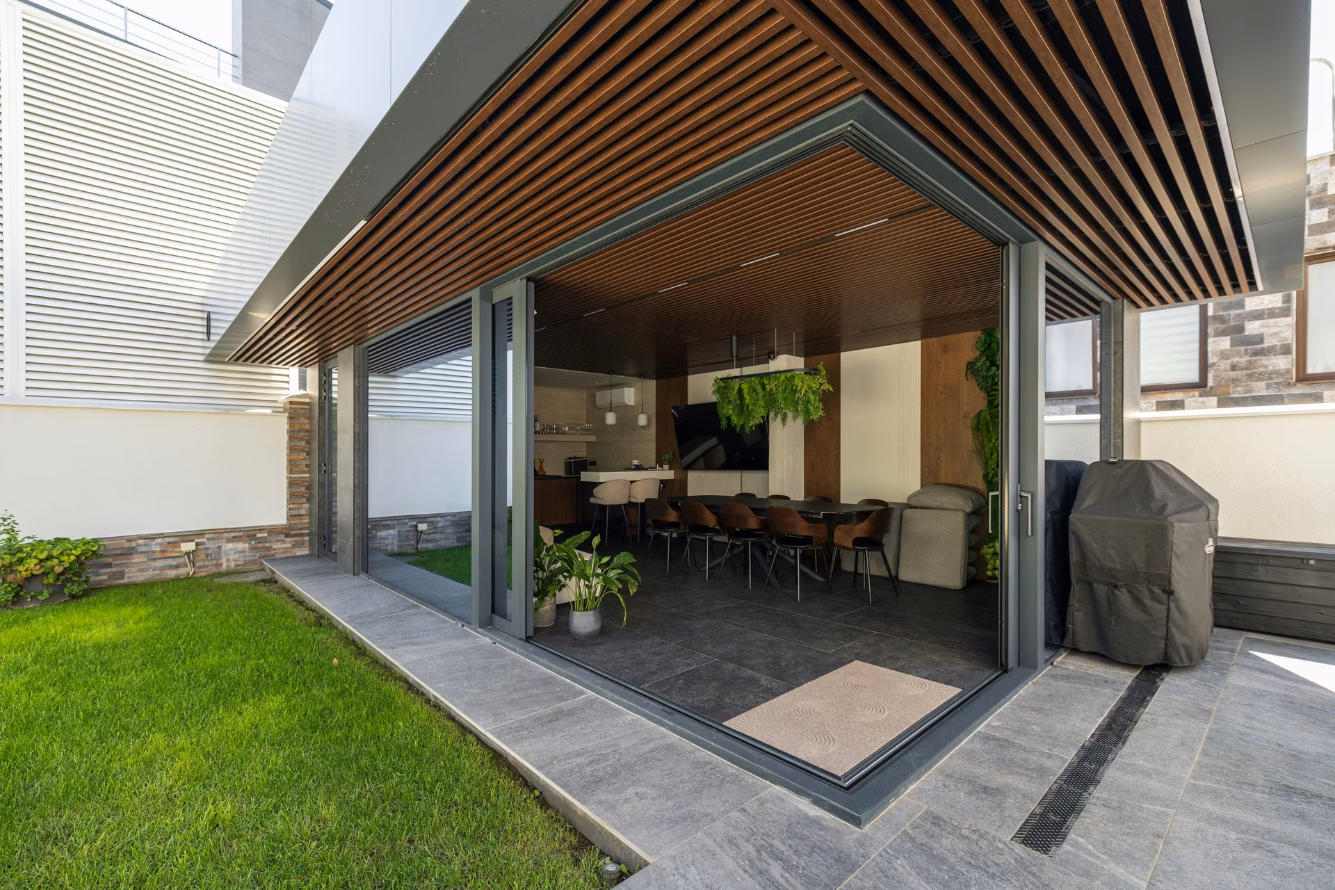A terrace where two panoramic sliding systems meet at 90 degrees, opening the corner completely and connecting the sheltered space with the pool and landscape.